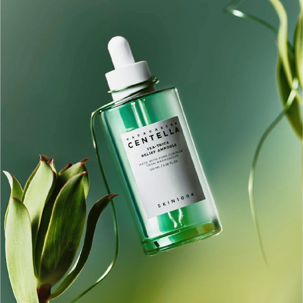 SKIN1004 Madagascar Centella Tea-Trica Relief Ampoule – grüne Glasflasche mit Pipette, weißem Etikett und 100 ml Inhalt, fotografiert vor grünem Hintergrund mit Pflanzendetails.