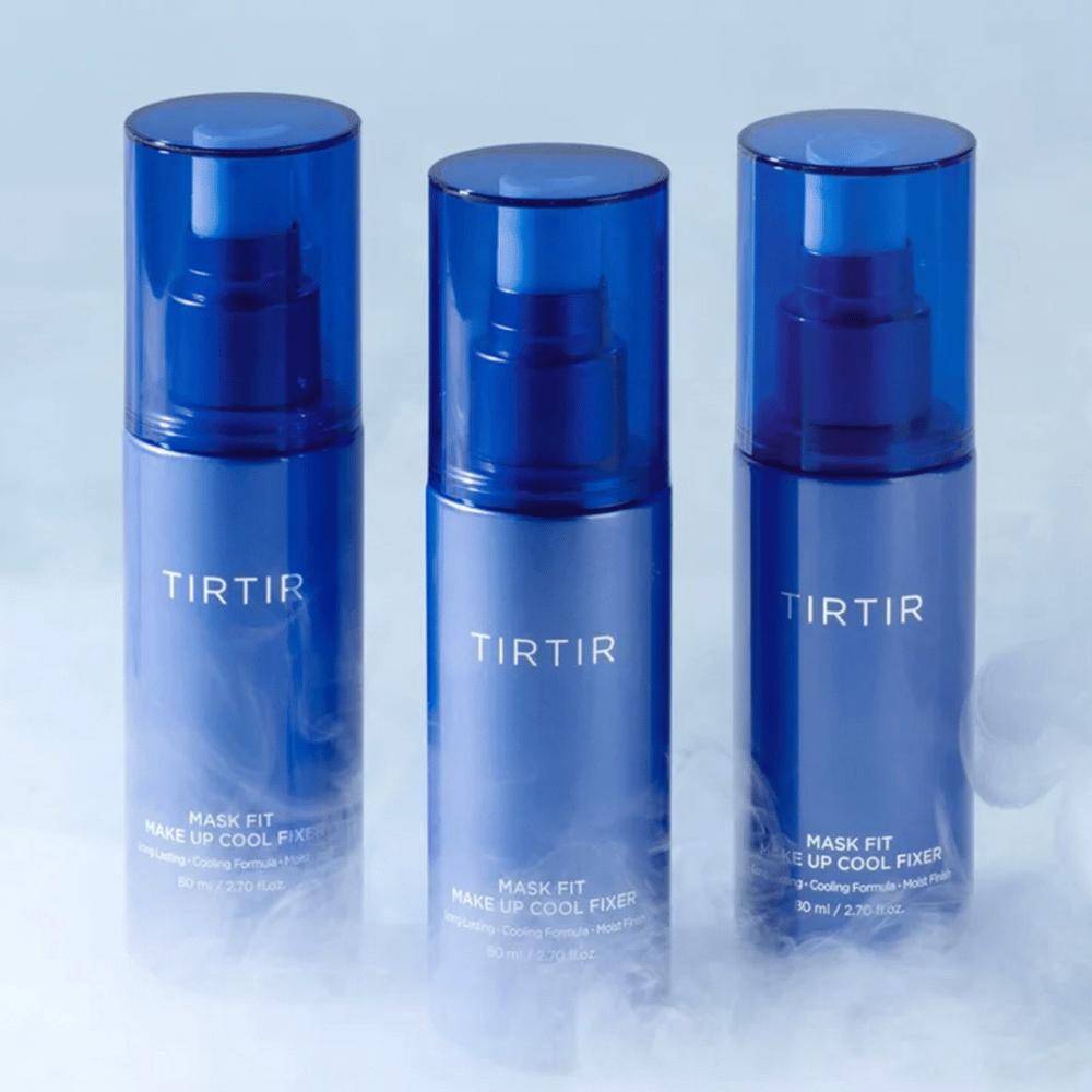 Drei blaue Sprühflaschen mit "TIRTIR Mask Fit Make Up Cool Fixer" auf dem Etikett. Jede Flasche fasst 80 ml (2,70 fl. oz.) und ist dafür ausgelegt, ein erfrischendes Gefühl und langanhaltendes Make-up zu bieten. Die Flaschen stehen auf einem hellen Hintergrund mit Nebel, um eine Atmosphäre der Frische zu schaffen.
