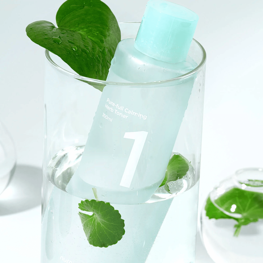 Eine Flasche mit No.1 Pure-Full Calming Herb Toner in einem Glas mit Wasser und grünen Blättern platziert. Die Flasche hat einen hellblauen Verschluss und ein Etikett mit der Aufschrift "Pure-full Calming Herb Toner" sowie "300ml". Das Produkt sieht frisch aus mit Wasser und Pflanzen im Hintergrund, was ein beruhigendes und natürliches Gefühl vermittelt.
