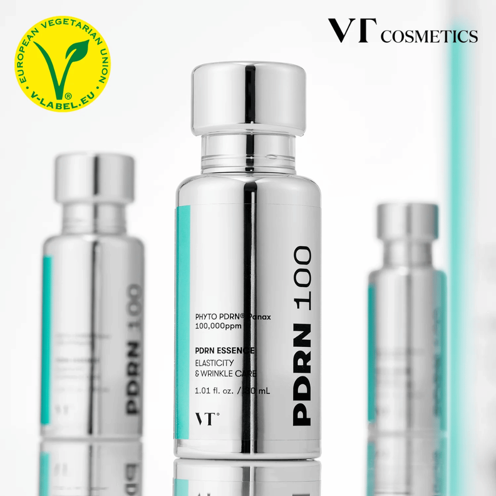 Mehrere silberfarbene Flaschen von VT PDRN 100 Essence stehen aufgereiht, mit klarer Kennzeichnung von 100.000 ppm PDRN und Fokus auf Elastizität und Faltenpflege. Oben ist das Logo von VT Cosmetics und ein V-Label für vegetarischen Inhalt zu sehen.