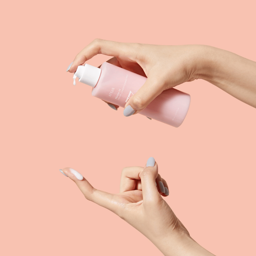Das Bild zeigt jemandes Hände, die eine Flasche mit ANUA Peach 77% Niacin Conditioning Milk halten. Dieses Hautpflegeprodukt scheint eine milchige Konsistenz zu haben und ist dafür ausgelegt, die Haut zu pflegen und ihren Zustand zu verbessern.