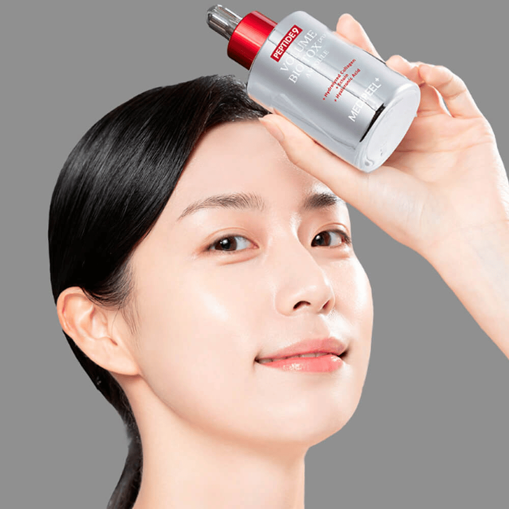 Person håller upp MEDI-PEEL Peptide 9 Volume Bio Tox Pro Ampoule mot pannan. Huden ser återfuktad och strålande ut – serumet stärker elasticitet och fasthet.