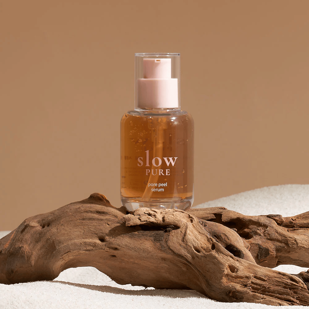 Slow Pure Pore Peel Serum auf Sand platziert mit Holzelement im Hintergrund, Symbol für natürliche Hautpflege.