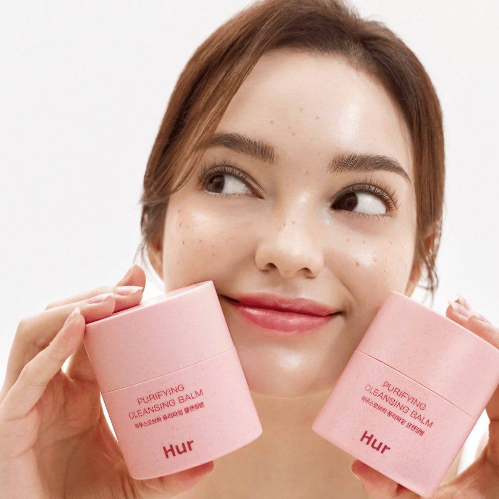 Modell hält zwei Dosen Wie Purifying Cleansing Balm. Milder Reinigungsbalsam, der für empfindliche Haut geeignet ist und ein frisches, hydratisiertes Gefühl nach der Reinigung verleiht.