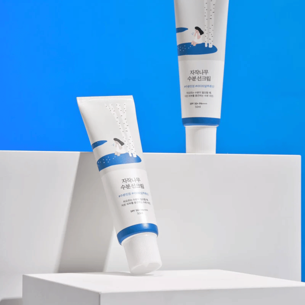 Zwei Tuben mit Round Lab Birch Juice Moisturizing Sunscreen SPF50+ PA++++ 50ml, die auf einem blauen Hintergrund stehen.