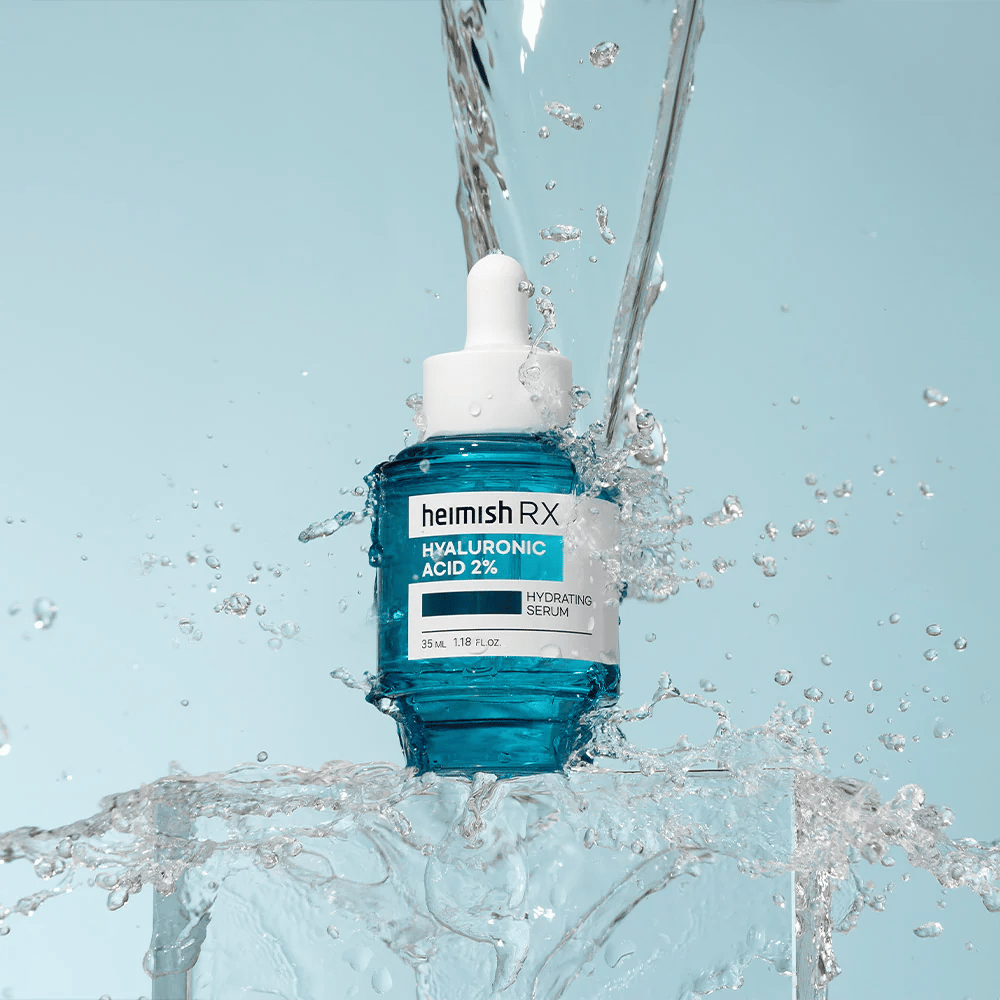 Heimish RX Hyaluronsäure 2% Feuchtigkeitsserum auf einer eisähnlichen Oberfläche mit spritzendem Wasser ringsum platziert, was intensive Feuchtigkeit und Frische symbolisiert.