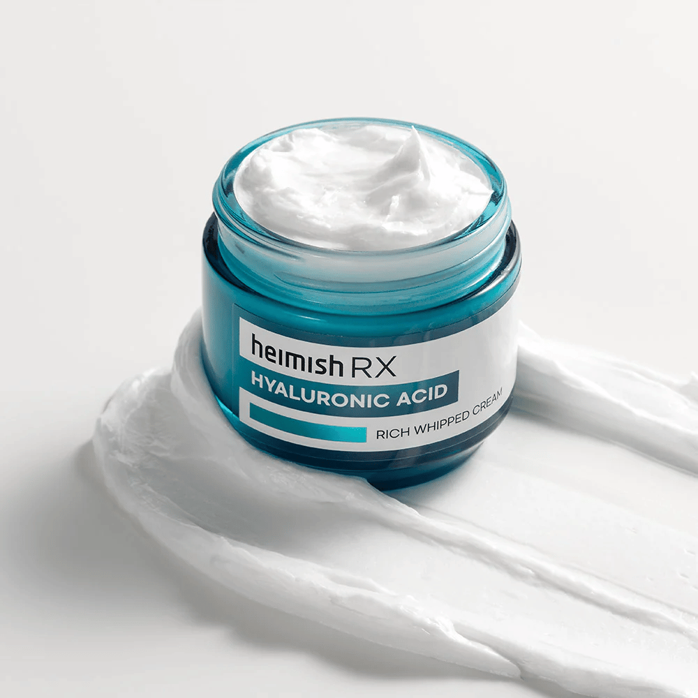 Heimish RX Hyaluronic Acid Rich Whipped Cream in einem blauen Glasgefäß mit reicher und fluffiger Konsistenz, auf einem weißen Hintergrund verteilt. Intensiv feuchtigkeitsspendende Gesichtscreme mit Hyaluronsäure für tiefe Feuchtigkeit und weiche Haut.