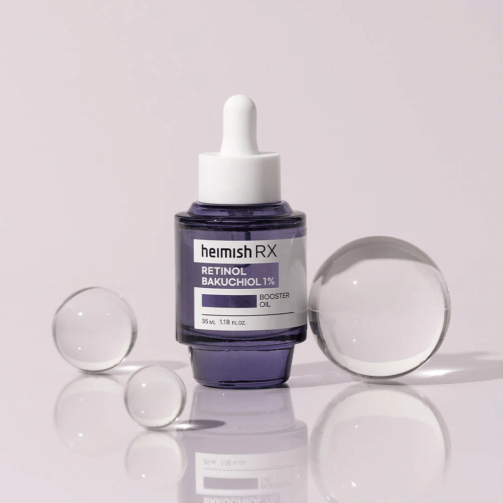Heimish RX Retinol Bakuchiol Booster Oil 1% in einer eleganten lila Glasflasche mit Pipette. Das Öl ist auf einer reflektierenden Oberfläche mit Glaskugeln herum platziert, was ein luxuriöses und modernes Gefühl vermittelt.