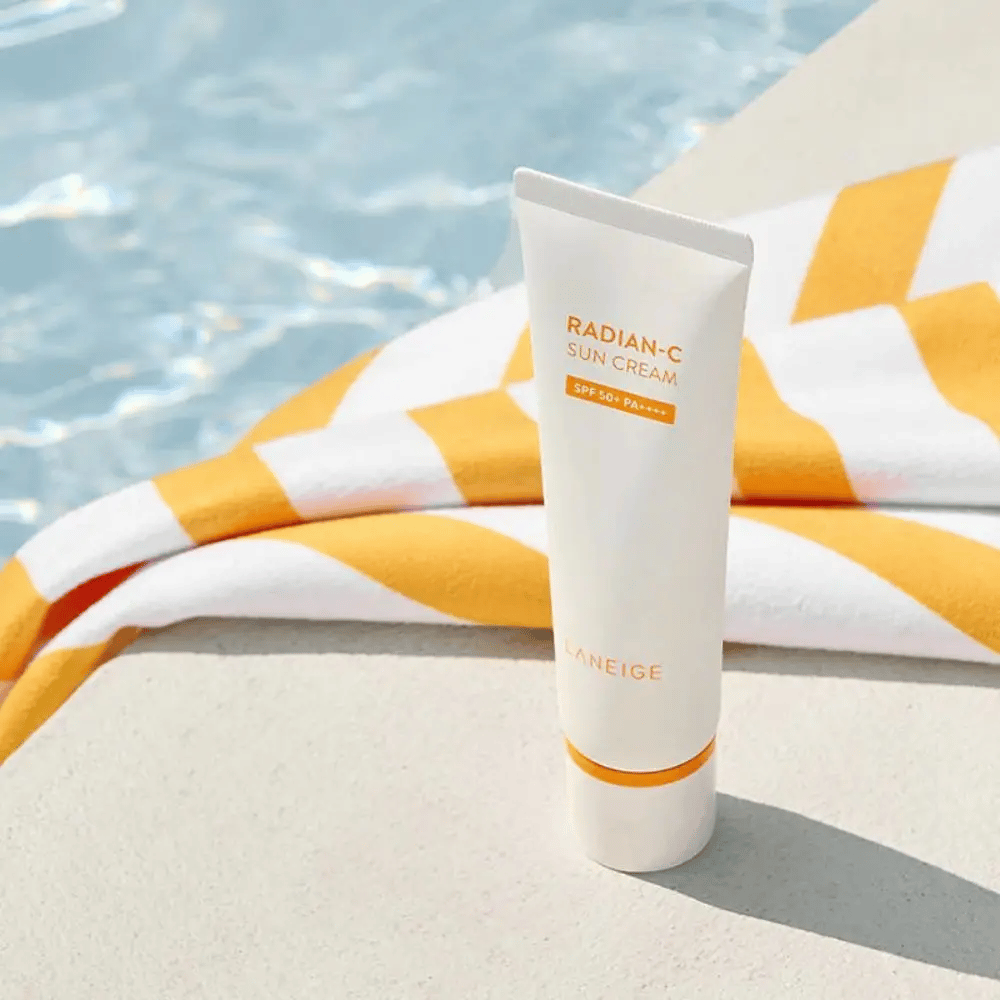 LANEIGE Radian-C Sun Cream steht am Poolrand mit einem gelb-weiß gestreiften Handtuch im Hintergrund.