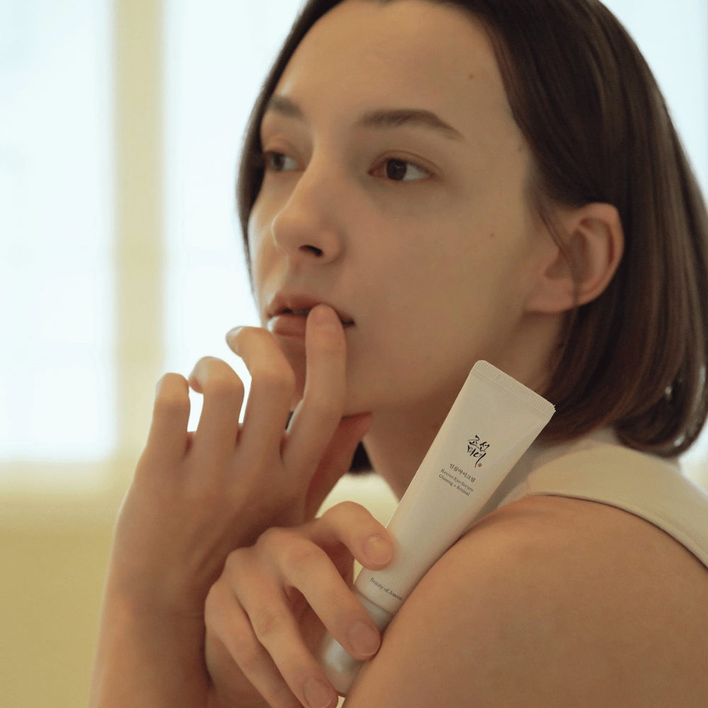 Modell hält Beauty of Joseon Revive Eye Serum und trägt es vorsichtig auf die Haut auf, um eine hydratisierte und glatte Augenkontur zu erzielen.
