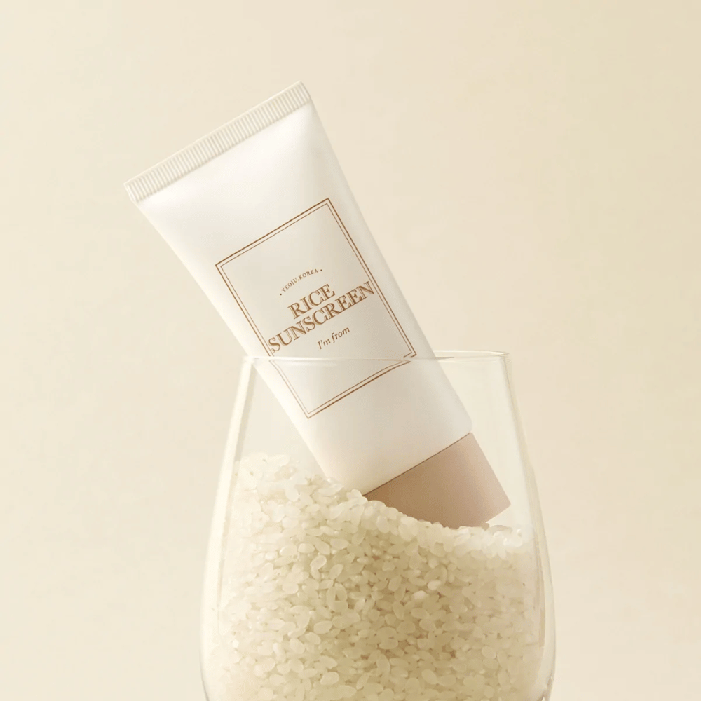 Tube mit "I'm from" Rice Sunscreen, SPF50+ PA++++, platziert in einem Glas mit Reiskörnern.