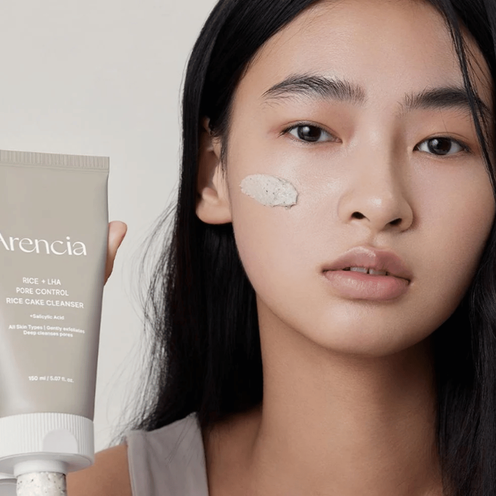 Modell, das Arencia Rice + LHA Pore Control Rice Cake Cleanser hält, mit aufgetragener Produkt auf der Wange, illustriert milde aber effektive Porenreinigung für den täglichen Gebrauch.