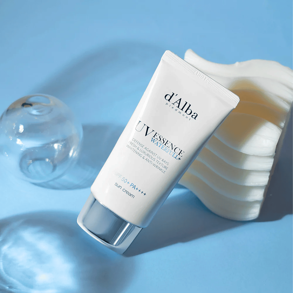 d'Alba UV Essence Waterfull+ Sun Cream mit SPF 50+ PA++++ liegt vor einem blauen Hintergrund mit Lichtreflexionen und dekorativen Elementen – hebt die frischen und feuchtigkeitsspendenden Eigenschaften der Sonnencreme hervor.