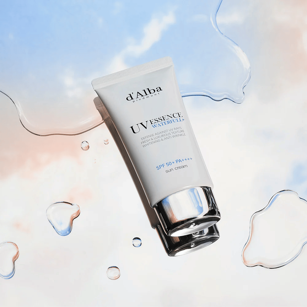 Produktbild von d'Alba UV Essence Waterfull+ Sun Cream mit SPF 50+ PA++++, platziert vor einem Hintergrund mit Wasserspritzern und blaurosa Himmel – symbolisiert leichten und feuchtigkeitsspendenden Sonnenschutz.
