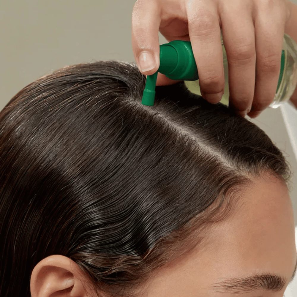 Eine Person trägt AROMATICA Rosemary Root Enhancer mit Hilfe der gezielten Düse direkt auf die Kopfhaut auf. Das Bild zeigt, wie das Produkt zur Kopfhautpflege und zur Stärkung der Haarwurzeln verwendet wird.