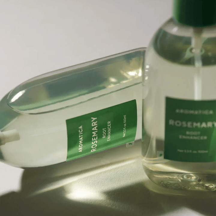 Zwei AROMATICA Rosemary Root Enhancer-Flaschen mit transparenter Schutzkappe und grünem Etikett. Nahaufnahme, die das Premiumdesign des Produkts und das natürliche Haarpflegekonzept hervorhebt.