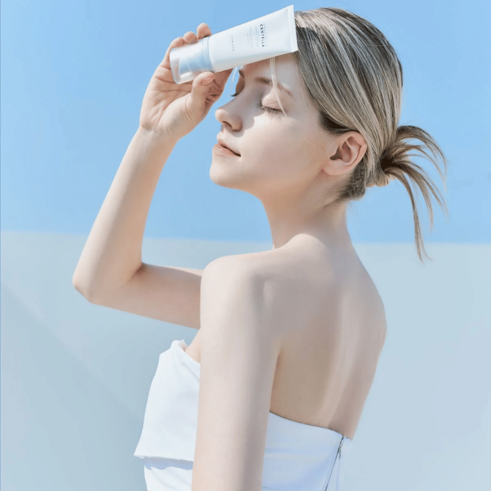 Eine Frau trägt SKIN1004 Madagascar Centella Hyalu-Cica Water-Fit Sun Serum 50ml auf, um das Gesicht vor UV-Strahlen zu schützen.