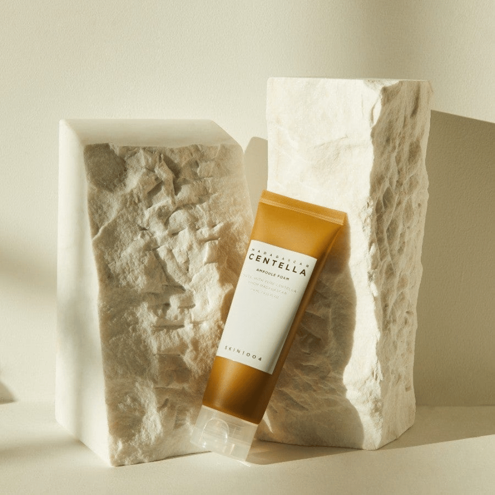 SKIN1004 Madagascar Centella Ampoule Foam stehend gegen helle Steinblöcke im natürlichen Sonnenlicht, mit ihrem braun-weißen Tubendesign und eleganter Minimalismus.