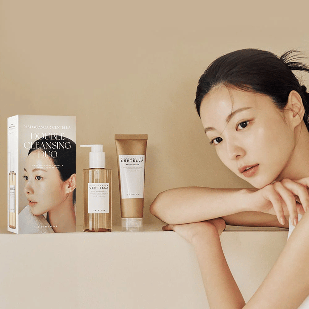 SKIN1004 Madagascar Centella Double Cleansing Duo Set mit Karton, ölbasierte Reinigung, Schaumreinigung und Modell mit befeuchteter Haut vor beigem Hintergrund.