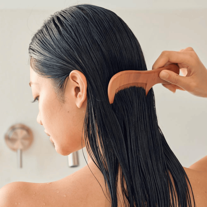 Eine Person kämmt langes, nasses Haar nach dem Auftragen von Heveblue Salmon Pullkeratin Centella Hair Treatment mit einem grobzinkigen Kamm durch. Veranschaulicht die entwirrende und weichmachende Wirkung für ein glatteres Ergebnis.