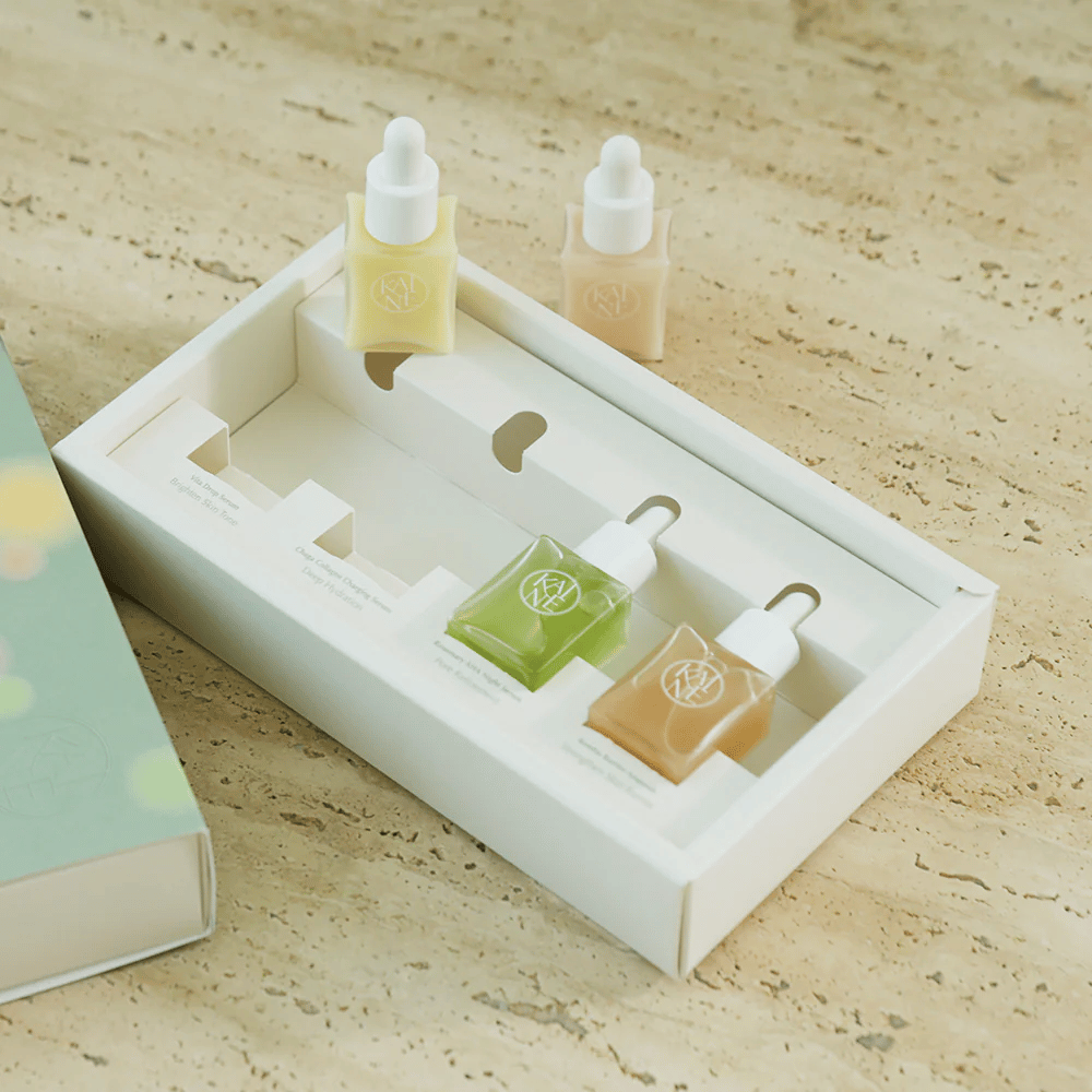 Vier bunte Serumflaschen von KAINE Serum Discovery Kit mit Pipettenverschluss, entworfen, um verschiedene Hautbedürfnisse in einer minimalistischen und stilvollen Verpackung zu erfüllen.