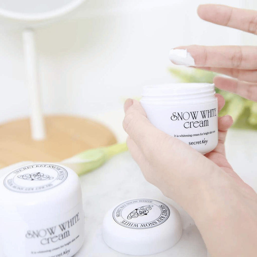 Hand, die weiße Creme aus einer Dose Secret Key Snow White Cream auf einem Schminktisch aufnimmt.