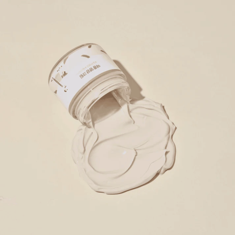 Mixsoon Soybean Nourishing Cream verschüttet aus dem Gefäß auf einem beigen Hintergrund. Die reichhaltige Konsistenz der Creme zeigt ihre intensiven feuchtigkeitsspendenden Eigenschaften.