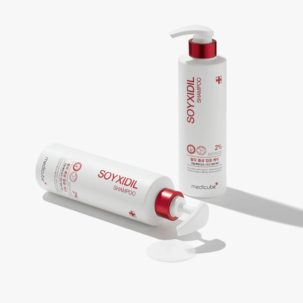 Zwei Flaschen von Medicube Soyxidil Shampoo im weißen und roten Design, eine stehend und eine liegend mit verschüttetem Shampoo daneben.