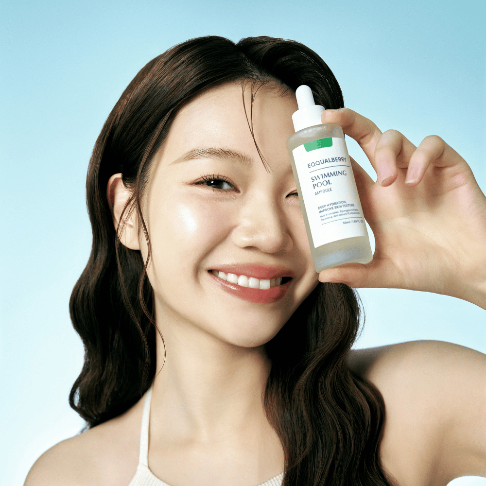 Eine lächelnde Frau hält Eqqualberry Swimming Pool Ampoule, ein Hautpflegeprodukt für intensive Feuchtigkeit, vor einem hellblauen Hintergrund.