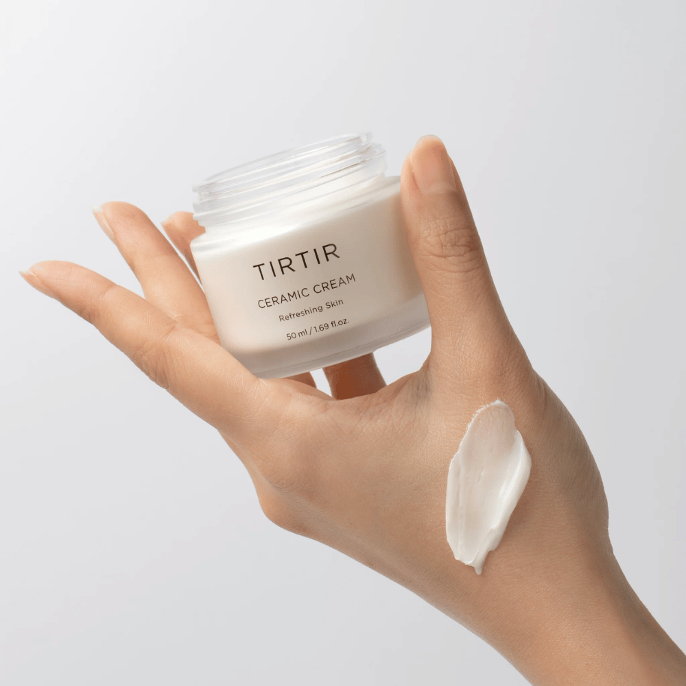 Eine Hand hält einen Behälter mit TIRTIR Ceramic Cream. Auf dem Handrücken wurde eine Menge der Creme aufgetragen. Die Creme scheint dick und feuchtigkeitsspendend zu sein. Die Verpackung gibt an, dass der Inhalt für "Refreshing Skin" ist und die Menge beträgt 50 ml / 1.69 fl oz.