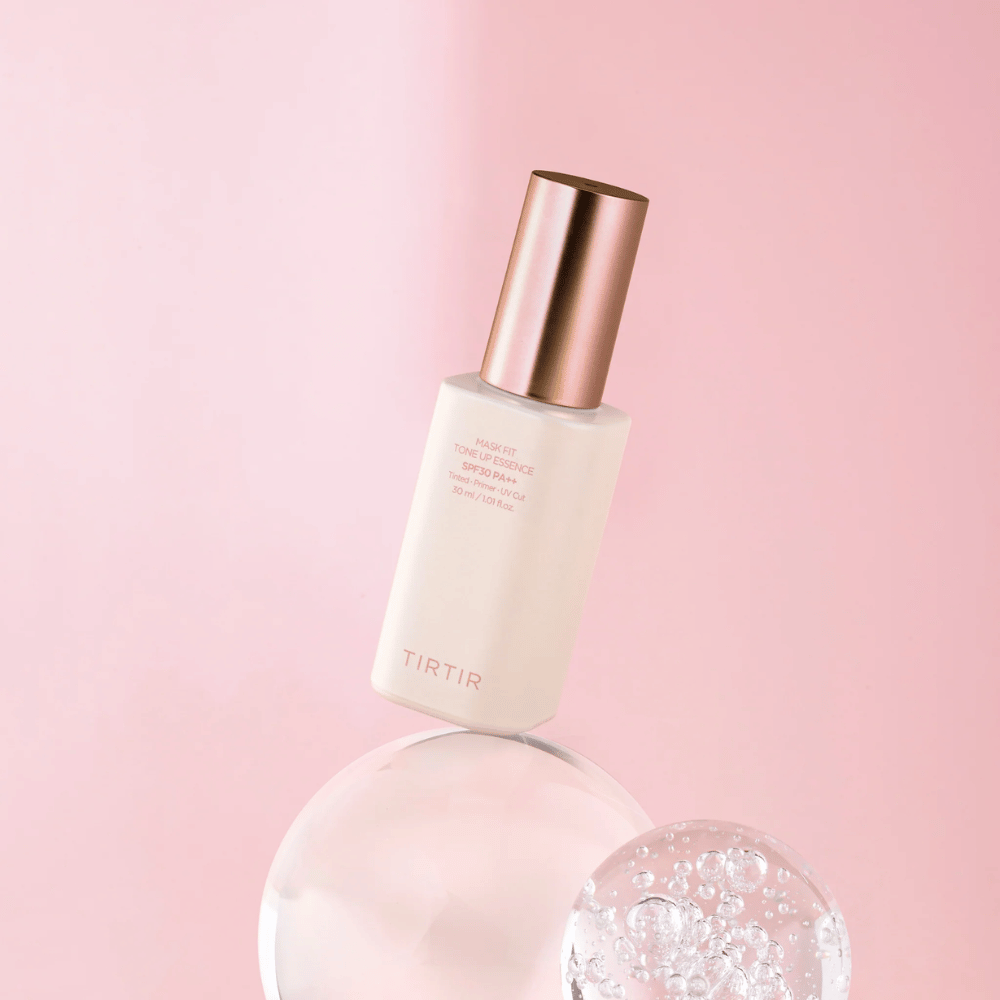 Das Bild zeigt eine Flasche "TIRTIR MASK FIT TONE UP ESSENCE" mit SPF30 PA++ vor einem rosa Hintergrund, was ein Gefühl von Weichheit und Femininität vermittelt.