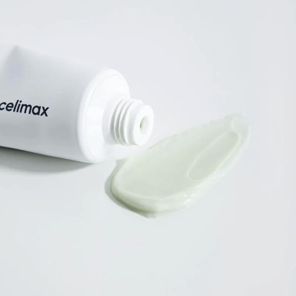 Celimax Noni Energy Repair Cream in einer weißen Tube mit einer kleinen Menge hellgrüner Creme, die neben der Tube auf einer weißen Oberfläche verteilt ist. Die Creme dient zur Pflege und Reparatur der Haut.
