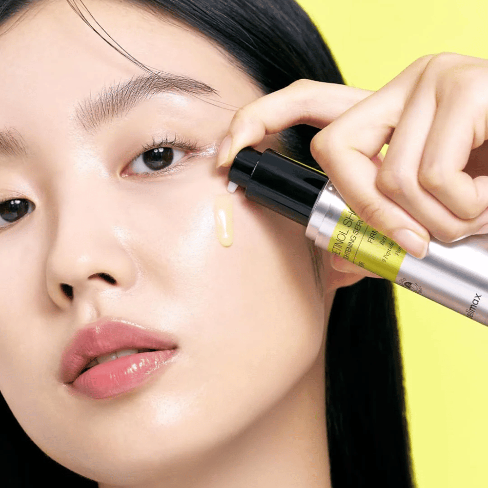 Modell trägt The Vita-A Retinol Shot Tightening Serum von Tiam in der Nähe des Augenbereichs auf, mit Fokus auf den Glanz der Haut und die gelbe Konsistenz des Serums.