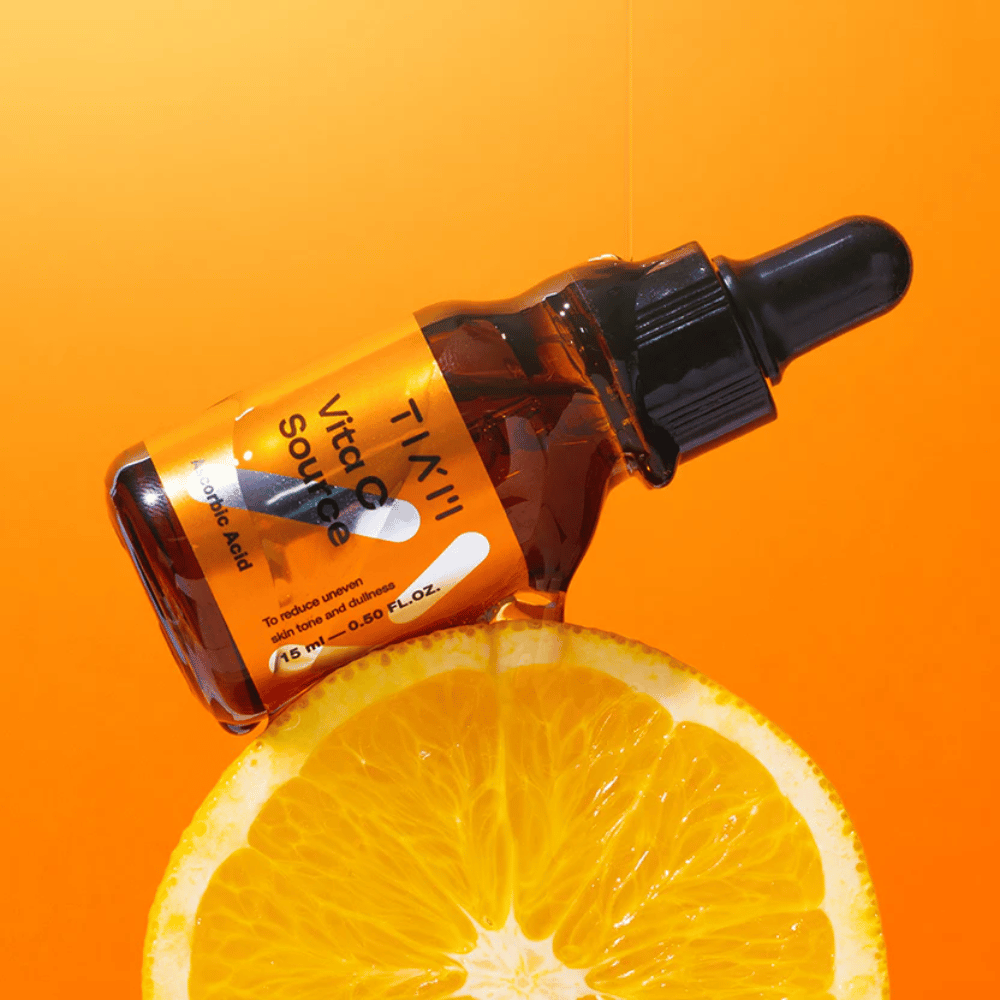 TIA'M Vita C Source-Flasche platziert vor einer Orange und einem orangefarbenen Hintergrund, der die Frische und antioxidative Wirkung von Vitamin C symbolisiert.