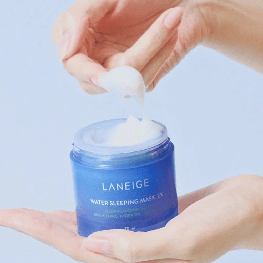 Eine Hand schöpft LANEIGE Water Sleeping Mask aus einer blauen Dose, mit Fokus auf die gelartige Konsistenz vor hellblauem Hintergrund.