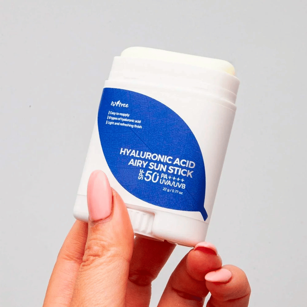 Eine Hand hält einen weißen Sonnenschutzstift mit blauem Etikett der Marke Isntree. Das Produkt heißt "Hyaluronic Acid Airy Sun Stick" und hat einen Lichtschutzfaktor von SPF 50+ PA++++.