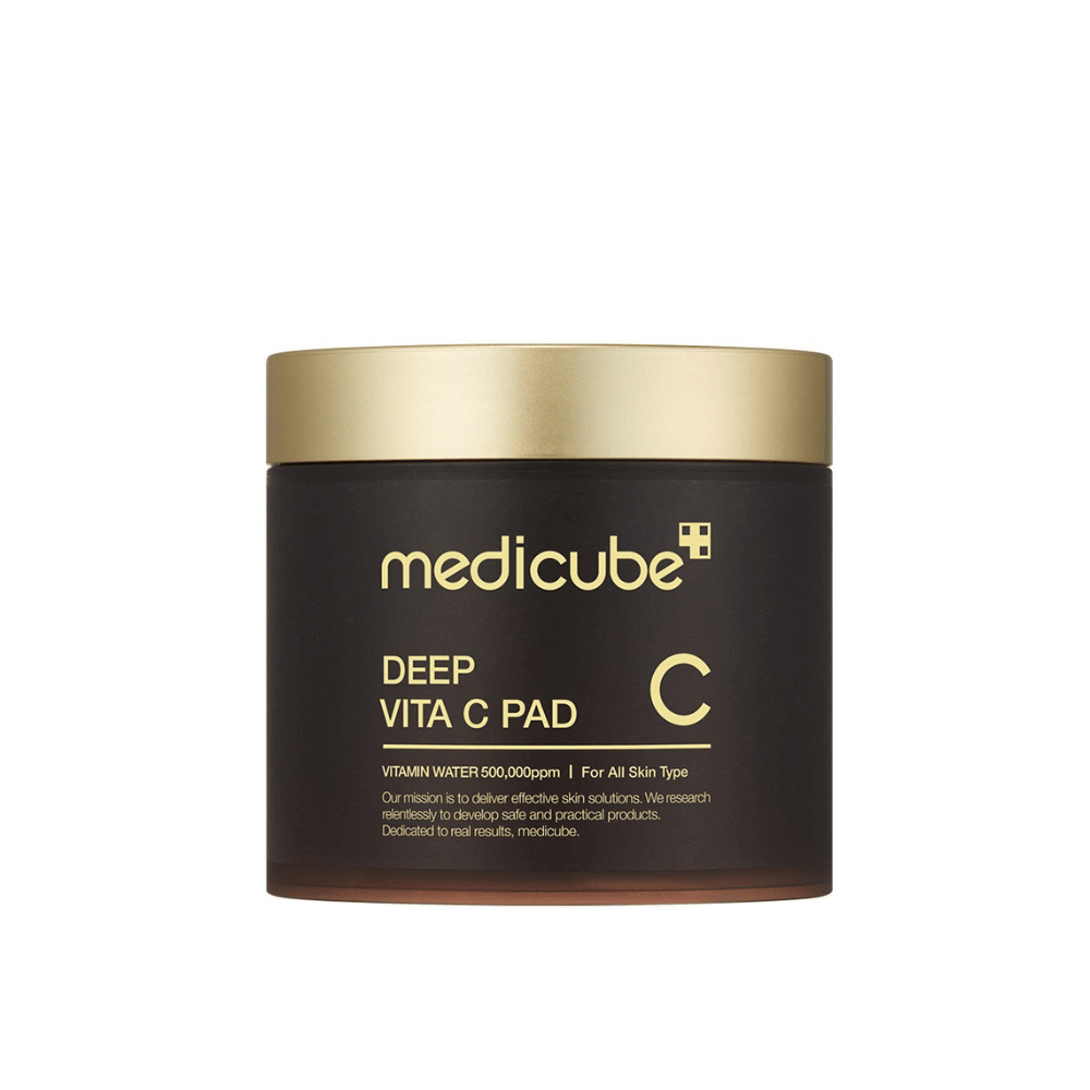 Eine Dose von medicube, mit der Aufschrift "Deep Vita C Pad", mit goldenem Deckel und dunklem Körper. Der Text auf der Dose gibt an, dass sie Vitamin C enthält und für alle Hauttypen geeignet ist. Der Hintergrund ist neutral.