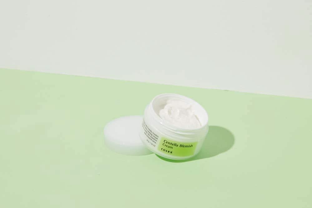 Ein Glas COSRX Centella Blemish Cream 30ml, das auf einer grünen Fläche steht.