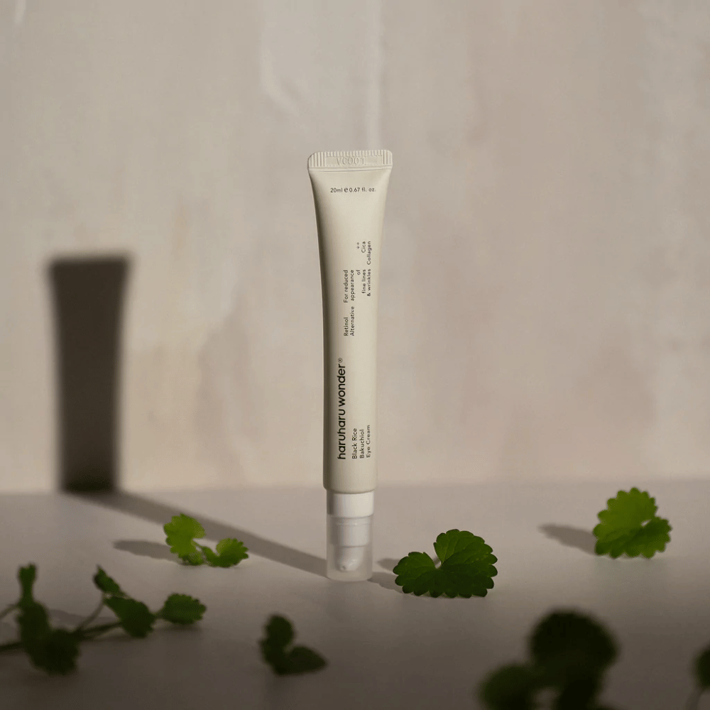 Eine Tube Haruharu Wonder Black Rice Bakuchiol Eye Cream 20ml umgeben von grünen Blättern, fokussiert auf die Sichtbarkeit von Falten und feinen Linien.