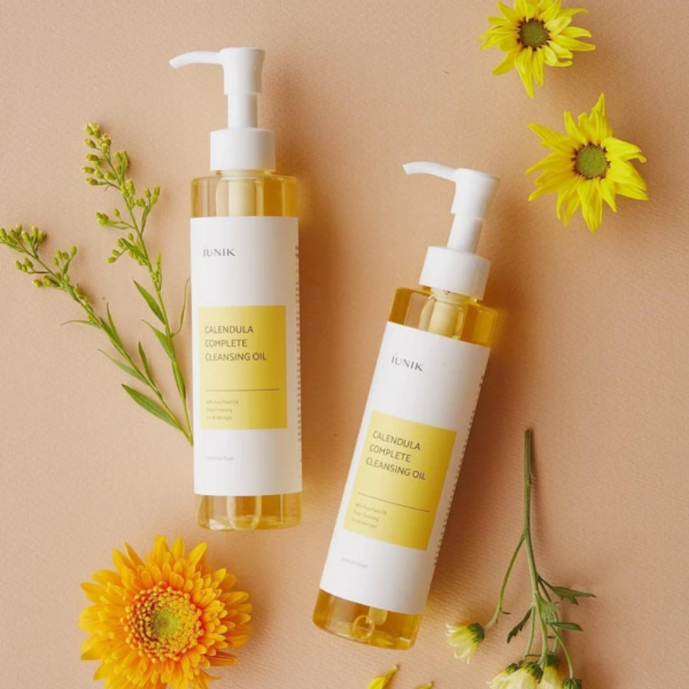 Zwei Flaschen iUNIK Calendula Complete Cleansing Oil 200ml mit gelben Blumen auf beigem Hintergrund, angereichert mit Pflanzenöl.