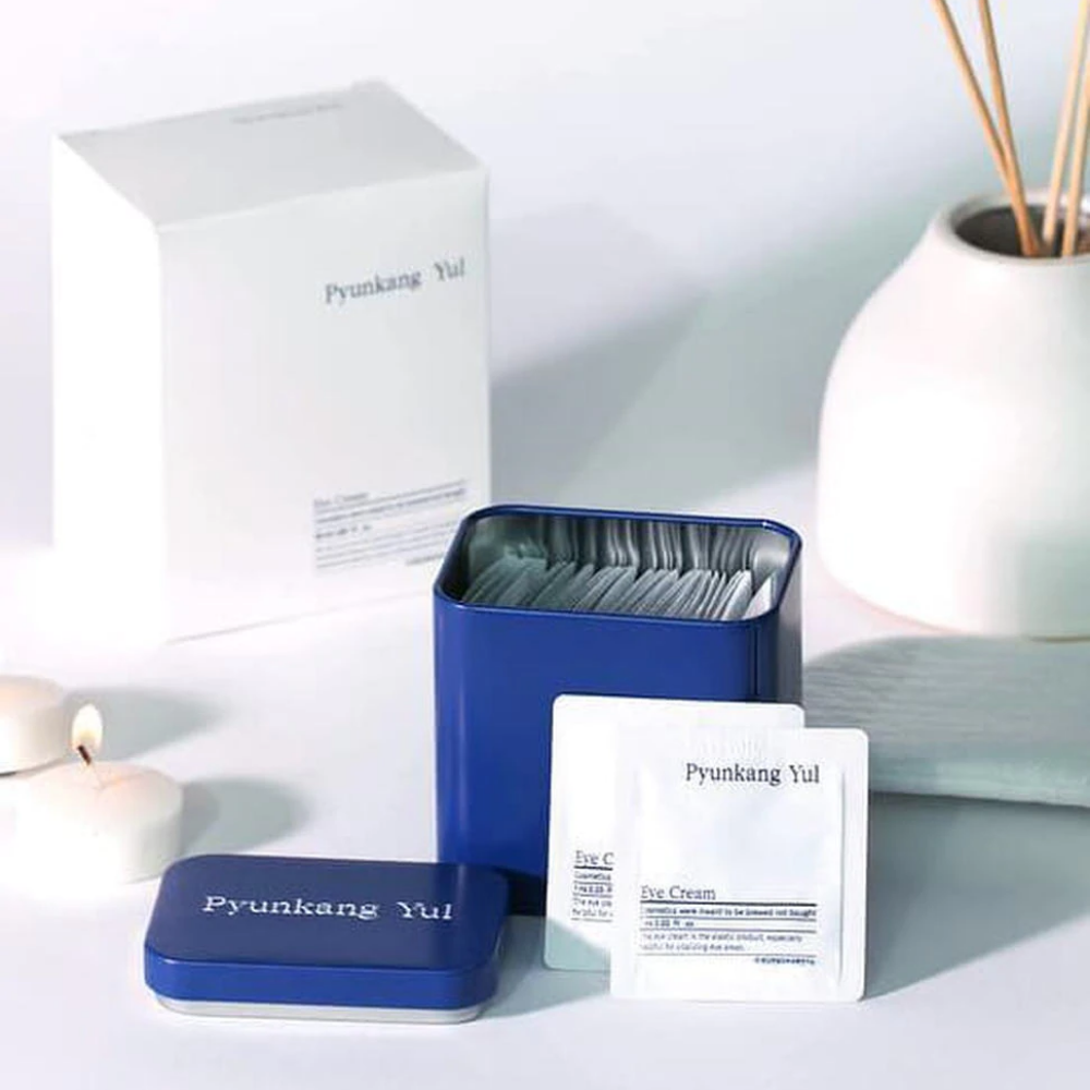 Eine weiße Schachtel mit blauem Deckel und Pyunkang Yul Augencreme 1ml x 50St daneben.