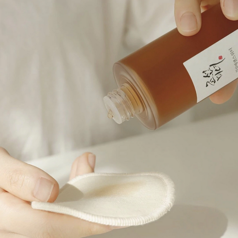 Eine Person, die Beauty of Joseon Ginseng Essence Water 150ml auf ein Tuch gießt, um trockene Haut zu behandeln und die Talgproduktion zu reduzieren.